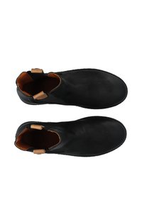 Bottines noires en cuir avec une texture lisse, bout arrondi et deux tirettes en cuir beige sur le col. L'intérieur est brun avec des détails de couture minimaux.