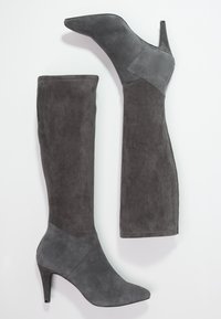 Bottes en daim grises au-dessus du genou avec un bout pointu et un talon haut et élancé ; texture lisse avec un design de panneau contrastant au niveau de la cheville.