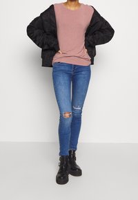 Giacca bomber nera, t-shirt rosa chiaro, jeans skinny blu strappati e stivali neri alla caviglia con fibbie. Tessuti morbidi e stili aderenti.