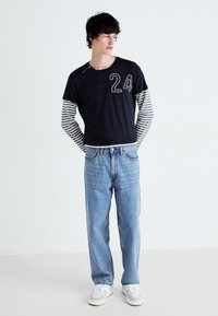 Marineblå t-shirt med korte ærmer og stribede lange ærmer samt "24" grafik, parret med lyseblå lige ben jeans og hvide sneakers.
