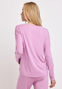 Długi rękaw, bluzka z okrągłym dekoltem z miękkiego różowego materiału. Charakteryzuje się luźnym krojem, delikatnymi detalami szycia oraz długimi rękawami.