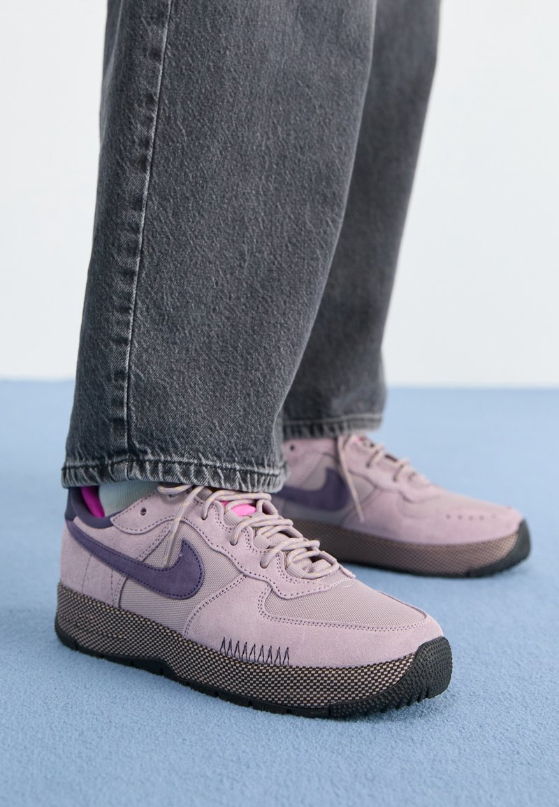 Baskets en daim rose et violet avec des semelles en caoutchouc noir, présentant une finition texturée, des lacets ronds et un logo swoosh prononcé.
