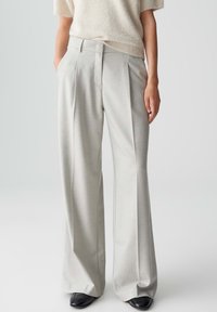 Pantalons larges taille haute gris clair avec des plis. Tissu lisse avec une coupe ajustée. Portés avec un pull ample de couleur crème.