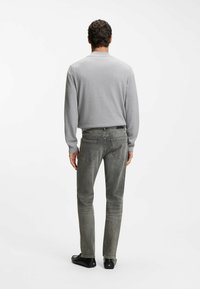 Szary sweter i jasnoszare dżinsy widziane od tyłu. Gładka tekstura o dopasowanym kroju. Czarne buty, minimalistyczne o smukłym kształcie.