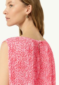 Różowa, bezrękawnikowa bluzka z teksturowanym, plisowanym tyłem i zapięciem na guziki, z wzorem w plamki w jasnoróżowych i ciemnoróżowych odcieniach.