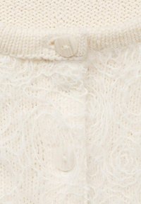 Cardigan crème tricoté avec un corps doux et texturé, un col côtelé et une fermeture ronde à bouton léger à l'avant.