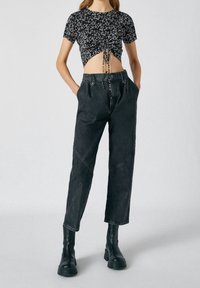 Haut court noir à motif floral avec un devant froncé et un détail noué, associé à un pantalon en jean noir taille haute avec une coupe ample et des coutures angulaires.