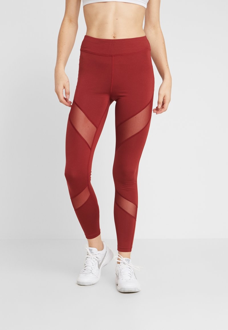 Leggings bordeaux con pannelli diagonali trasparenti, vita alta e un design aderente. Abbinati a scarpe da ginnastica bianche. Texture liscia.