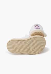 Zapato sin cordones de tela blanca con suela de goma beige texturizada. Presenta un parche colorido de un mono en el talón y está etiquetado como "Hecho en España".