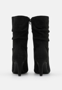 Bottes noires en daim montantes jusqu'aux genoux avec un design froissé, des fermetures éclair latérales et un talon effilé. Texture lisse avec une finition mate.