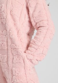 Roze fleece jumpsuit met gestructureerd patroon, bestaande uit een zachte, pluche stof, geribbelde manchetten en zijzakken voor extra functionaliteit.