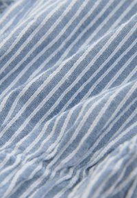 Gros plan sur un tissu rayé bleu et blanc avec un détail élastique froncé créant des plis doux et une texture.