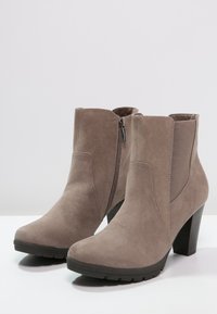 Beige mockasin stövlar med sidodragkedja, elastiska insatser och en tjock svart klack. Texturerad yta med en slät finish.