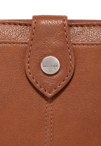 Brauner Leder-Geldbeutel mit strukturiertem Außenmaterial, genähten Akzenten und einem silbernen Druckknopf mit dem Wort "MAÎTRE."