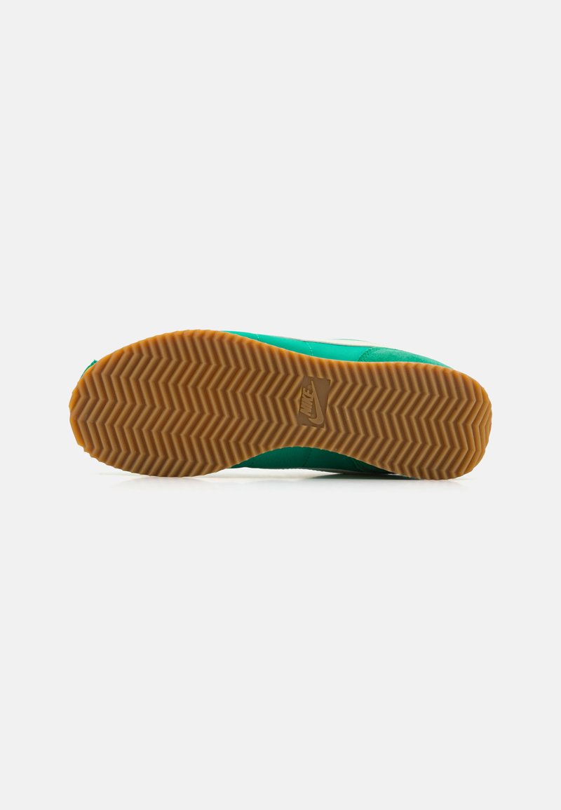 Zapatilla verde con una suela de goma texturizada que presenta un patrón de espiga; plantilla con marca; diseño elegante y construcción acolchada.