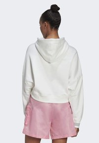 Sudadera corta blanca con capucha, de textura suave y silueta oversize, acompañada de pantalones cortos rosas con bolsillos y un acabado suave.