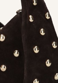 Zwarte suède handtas met gouden studs, met een gestructureerd oppervlak en een unieke vorm die een bovenhandvat omvat.