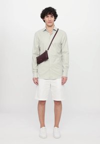 Cămașă călcată de culoare verde deschis, pantaloni scurți albi și adidași albi. Este purtată o poșetă crossbody burgundă cu un accent de fermoar argintiu.