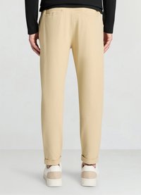 Beige leichte Hose mit lockerem Schnitt, ausgestattet mit zwei Gesäßtaschen und umgeklappten Bündchen, kombiniert mit weißen und beigen Sneakers.