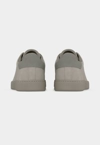 Paire de baskets décontractées grises vues de dos, avec col rembourré et semelle en caoutchouc plate sur un fond uni.