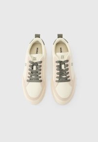 Zapatillas deportivas blancas con acentos de ante beige, puntera redonda y cordones grises. Presentan una lengüeta para tirar y una plantilla con marca. Textura suave.