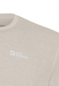 Nahaufnahme eines beigen Jack Wolfskin T-Shirts mit Rundhalsausschnitt und Logo im linken Brustbereich.