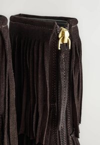 Botas de ante marrón oscuro con detalles de flecos a los lados, y un acento de cremallera dorada. La textura parece suave y aterciopelada.