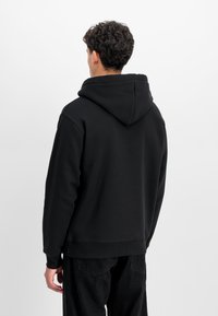 Sudadera negra hecha de una tela suave, con una gran capucha, puños acanalados y un ajuste relajado. Combinada con pantalones negros a juego.