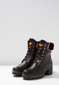 Stivaletti neri in pelle con colletto in pelliccia sintetica, dettagli in oro, laccio frontale e tacco spesso. Presenta una suola in gomma testurizzata per una buona aderenza.