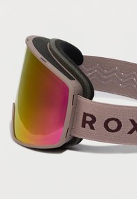 Ski brilles ar rozā un dzeltenu atstarojamo lēcu, bēšīgu rāmi, melnu putu oderi un bēšīgu elastīgu siksniņu ar "ROXY" tekstu.