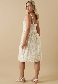 Kwiatowa midi sukienka z cienkimi, regulowanymi ramiączkami, marszczonym tyłem, kremową bazą i pomarańczowymi kwiatami. Noszona z białymi sandałkami na paski.