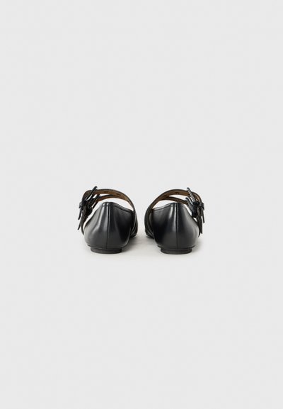 Ballerines en cuir noir avec un bout arrondi et un petit talon, dotées d'un accent de nœud décoratif sur la bride de cheville. Texture lisse et design simple.