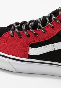 Baskets en suède noir et rouge avec une tige texturée rouge en toile, une bande latérale blanche et des lacets à motifs noir et blanc. Semelle en caoutchouc.