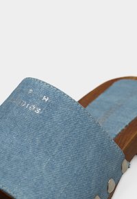 Μπλε τζιν κλογκ με ξύλινη σόλα και μεταλλικά καρφιά, πλάγια όψη που αναδεικνύει την υφή και τις λεπτομέρειες της ραφής.