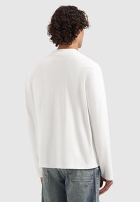 Weißes Langarmhemd aus weichem Stoff, mit lockerer Passform und einem einfachen Design ohne sichtbare Muster oder Logos.