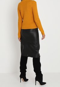 Pomarańczowy sweter z dzianiny z teksturowanym wzorem, zestawiony z czarną ołówkową spódnicą ze skóry z tylnym rozcięciem, noszony z czarnymi botkami na szpilce.