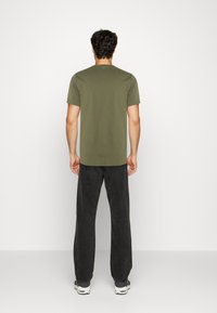 Olive green short-sleeve t-shirt, cotton material, crew neck, paired with black wide-leg trousers, featured from the back view.