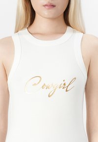 Hvit ribbestrikket singlet med gullfarget, skråskrift "Cowgirl" print over brystet. Glatt tekstur med tettsittende design og vide ermehull.