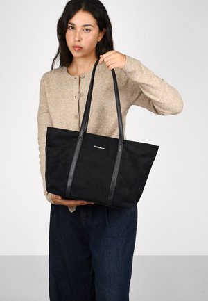 Bolso de mano negro con textura de ante suave, que cuenta con dos asas de cuero, diseño minimalista y un logo sutil en la parte frontal.