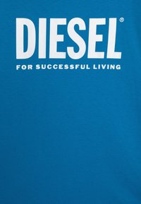 Modré bavlněné tričko s velkým bílým textem "DIESEL" a "PRO ÚSPĚŠNÝ ŽIVOT", s hladkou texturou a designem s kulatým výstřihem.