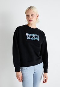 Čierna mikina so zeleno-modrým kvetinovým logom Levi's na prednej strane. Má dlhé rukávy, okrúhly výstrih a rebrované manžety.