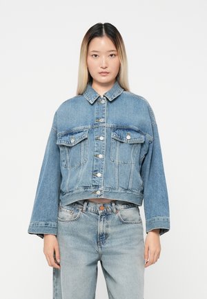 Kuttet denimjakke i lys blå, med krage, knappestengning foran og to brystlommer med klaff. Vidde ermer og myk tekstur.