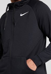 Felpa nera con zip e colletto alto, con logo Nike riflettente sul petto, polsini elasticizzati e tasche frontali. Tessuto dalla consistenza morbida.
