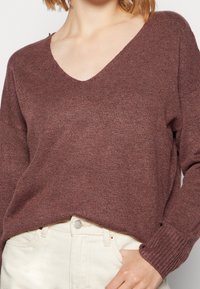 Mörkröd v-ringad tröja med en texturerad stickdesign, långa ärmar och ribbade ärmslut. Matchad med ljusa jeans med en silverknapp.