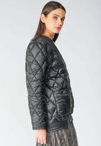 Veste matelassée noire avec un col rond, dotée d'une fermeture à boutons sur le devant, de poches latérales et d'un ourlet texturé. Matériau synthétique lisse.