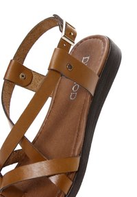 Sandal in pelle marrone con cinturini incrociati e chiusura a fibbia. Presenta una suola testurizzata di un marrone più scuro e un plantare liscio.