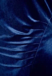 Tissu en velours bleu marine avec une texture douce, présentant des sections froncées et un léger éclat. Le design met en valeur de magnifiques plis.