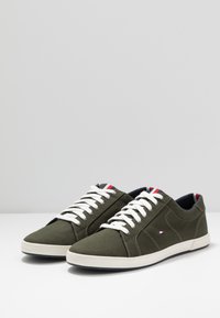 Gröna canvas-sneakers med vita snören, gummisulor och marinblå foder. Har röda, vita och blå detaljer på tungan.