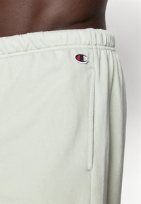 Light green sweatpants made of soft, textured fabric. Features an elastic waistband and a small embroidered logo on the side.