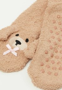 Braune, flauschige Socken mit einem Bärenmotiv; verfügen über ein strukturiertes Bärenface, schwarze Stickereien und eine pinkfarbene Schleife. Die Unterseite hat gummierte Grip-Punkte.